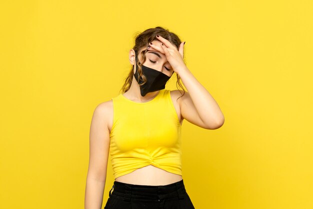 Vista frontal de la mujer joven con dolor de cabeza en la pared amarilla