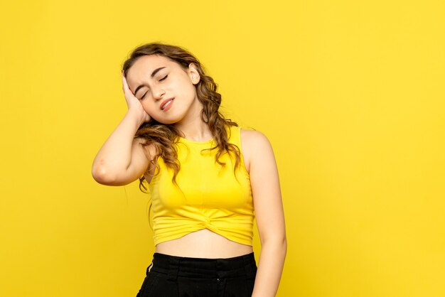 Vista frontal de la mujer joven con dolor de cabeza severo en la pared amarilla