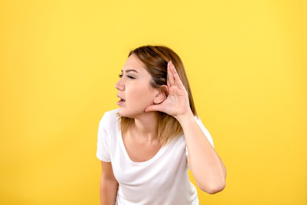 Vista frontal, de, mujer joven, escuchar, en, pared amarilla