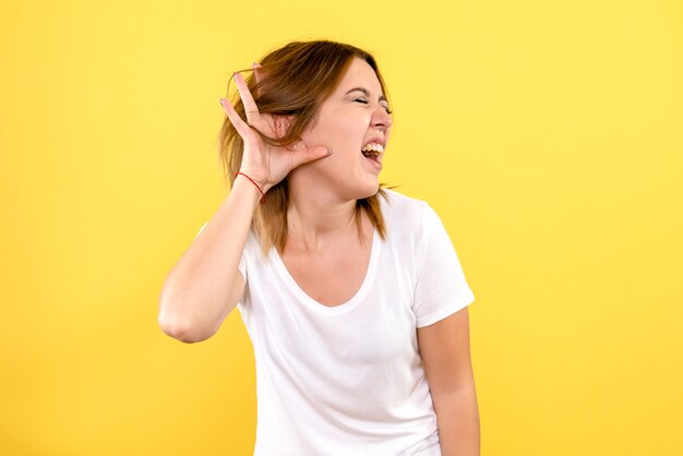 Vista frontal, de, mujer joven, escuchar, en, pared amarilla