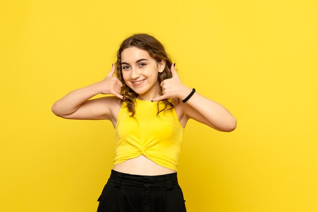 Vista frontal de la mujer joven con expresión sonriente en la pared amarilla