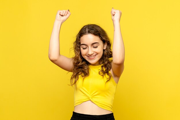 Vista frontal de la mujer joven felizmente regocijándose en la pared amarilla