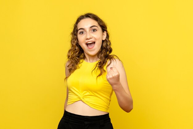 Vista frontal de la mujer joven felizmente regocijándose en la pared amarilla