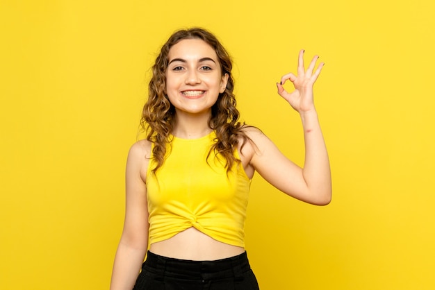 Foto gratuita vista frontal, de, mujer joven, felizmente, sonriente, en, pared amarilla