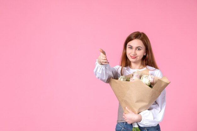 Vista frontal mujer joven con flores como presente el día de la mujer sobre fondo rosa fecha de marzo femenina horizontal igualdad rosa amor sensual