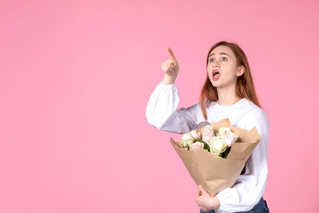 Vista frontal mujer joven con flores como presente el día de la mujer sobre fondo rosa marzo femenino horizontal amor mujer sensual fecha rosa