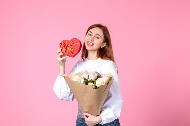 Vista frontal mujer joven con flores y presente como regalo del día de la mujer sobre fondo rosa marcha horizontal igualdad amor sensual femenino fecha rosa mujer