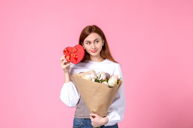 Vista frontal mujer joven con flores y presente como regalo del día de la mujer sobre fondo rosa marzo horizontal igualdad amor femenino fecha rosa mujer