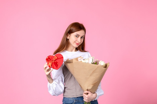Vista frontal mujer joven con flores y presente como regalo del día de la mujer sobre fondo rosa marzo horizontal igualdad amor sensual fecha rosa mujer
