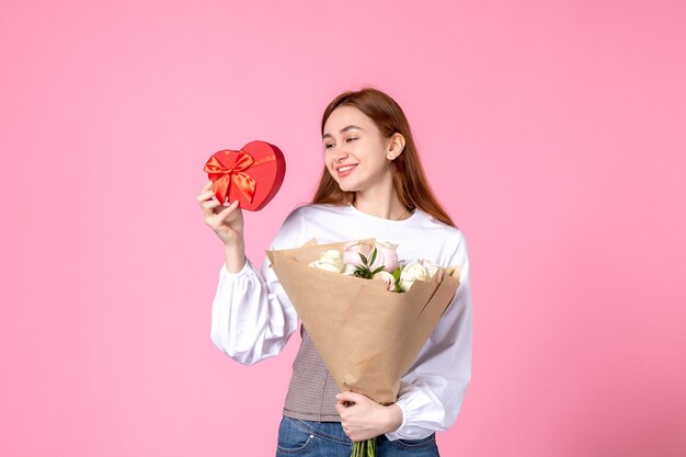 Vista frontal mujer joven con flores y presente como regalo del día de la mujer sobre fondo rosa marzo horizontal mujer fecha igualdad rosa amor femenino