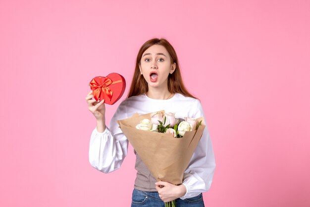 Vista frontal mujer joven con flores y presente como regalo del día de la mujer sobre fondo rosa marzo horizontal mujer fecha igualdad rosa sensual femenino