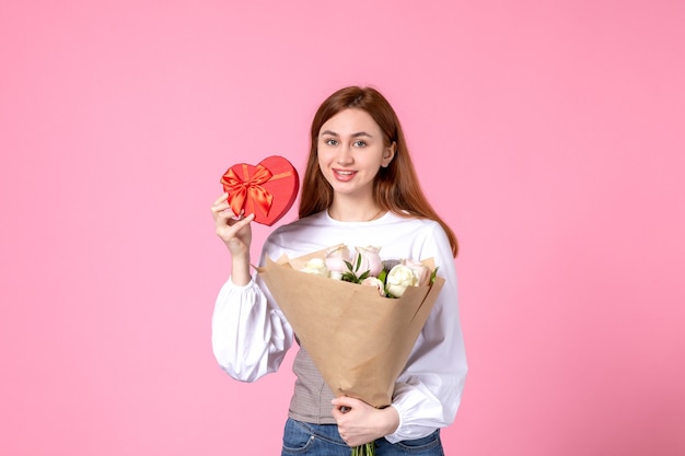Vista frontal mujer joven con flores y presente como regalo del día de la mujer sobre fondo rosa marzo horizontal mujer igualdad rosa amor sensual fecha femenina