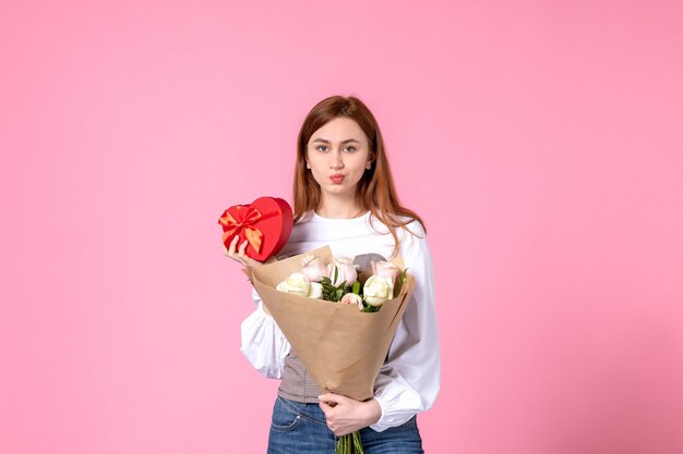 Vista frontal mujer joven con flores y presente como regalo del día de la mujer sobre fondo rosa rosa marzo horizontal fecha femenina mujer amor igualdad