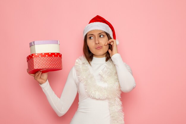 Vista frontal de la mujer joven en gorra roja con regalos en forma de corazón en la pared rosa