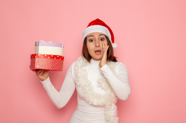 Vista frontal de la mujer joven en gorra roja con regalos en forma de corazón en la pared rosa