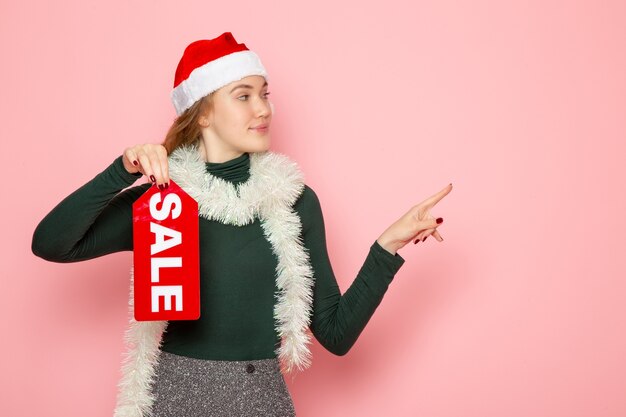 Vista frontal de la mujer joven en gorra roja con venta escrito en pared rosa