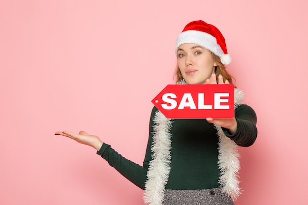 Vista frontal de la mujer joven en gorra roja con venta escrito en pared rosa