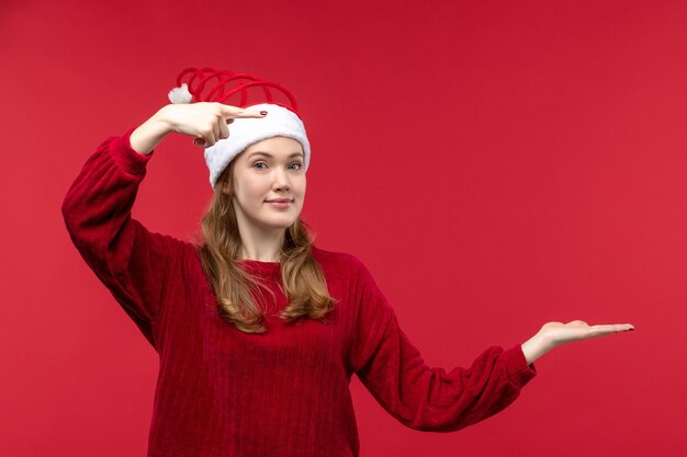 Vista frontal mujer joven en gorro rojo de navidad en el piso rojo vacaciones de mujer roja