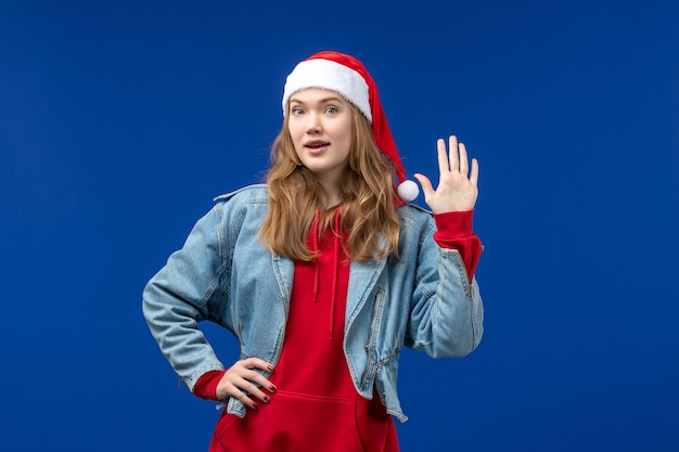 Vista frontal mujer joven con gorro rojo de navidad sobre fondo azul claro emoción color navideño