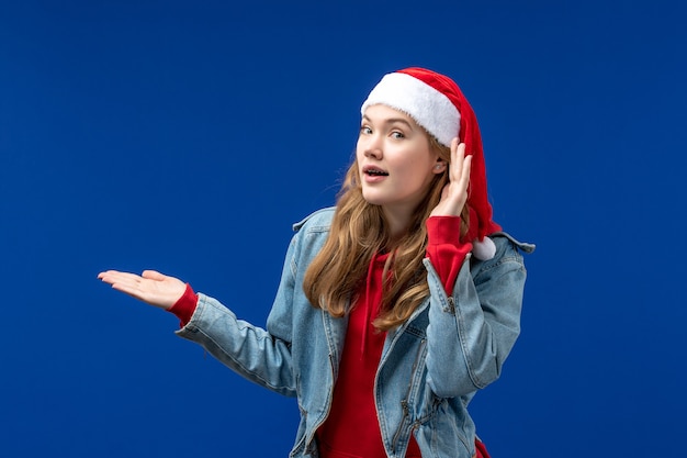 Vista frontal mujer joven en gorro rojo de navidad sobre un fondo azul color de emociones navideñas