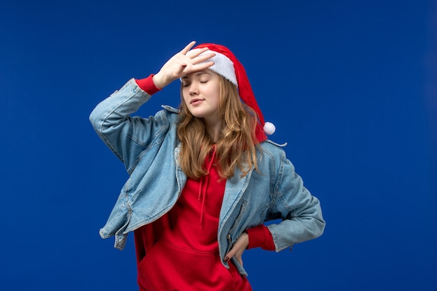 Vista frontal mujer joven con gorro rojo de navidad sobre fondo azul color de emociones navideñas