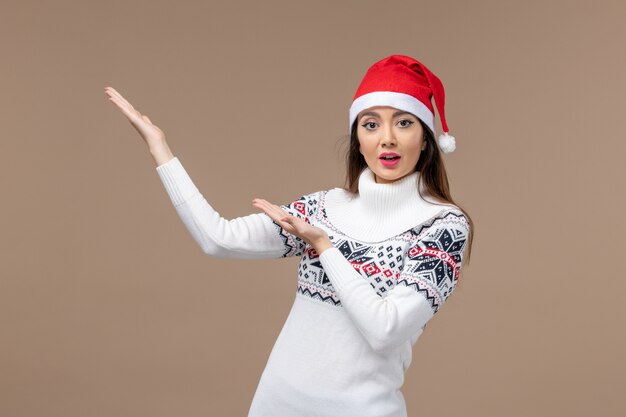 Vista frontal mujer joven con gorro rojo de navidad sobre fondo marrón emociones navideñas año nuevo