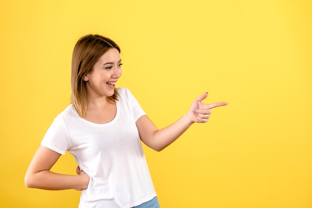 Vista frontal de la mujer joven hablando con alguien en la pared amarilla