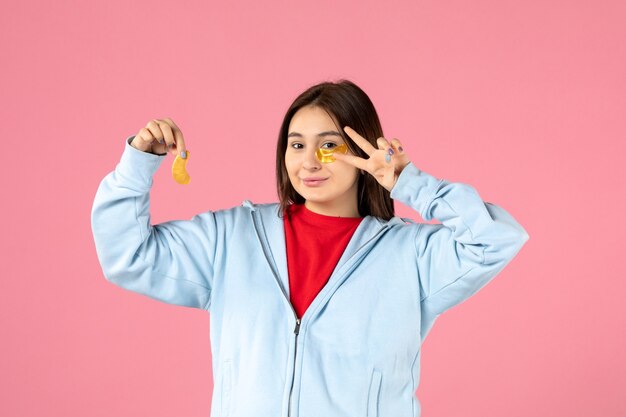 Vista frontal de la mujer joven haciendo una mascarilla en la pared rosa