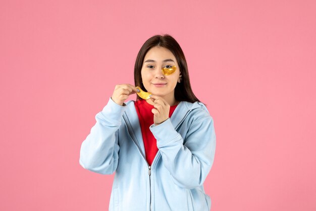 Vista frontal de la mujer joven haciendo una mascarilla en la pared rosa