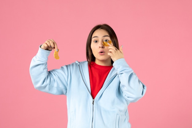 Vista frontal de la mujer joven haciendo una mascarilla en la pared rosa