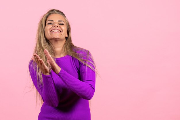 Vista frontal de una mujer joven en un hermoso vestido morado posando en la pared rosa