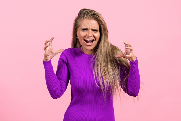 Vista frontal de una mujer joven en un hermoso vestido morado posando en la pared rosa