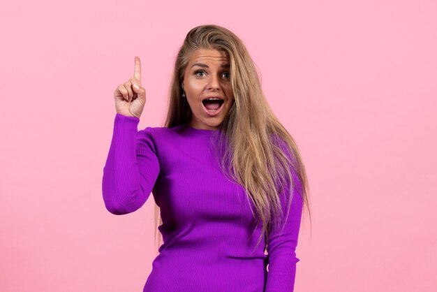 Vista frontal de una mujer joven en un hermoso vestido morado posando en la pared rosa