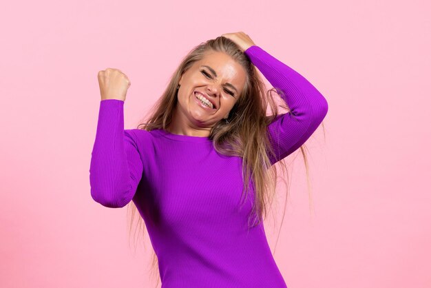 Vista frontal de una mujer joven en un hermoso vestido morado posando en la pared rosa