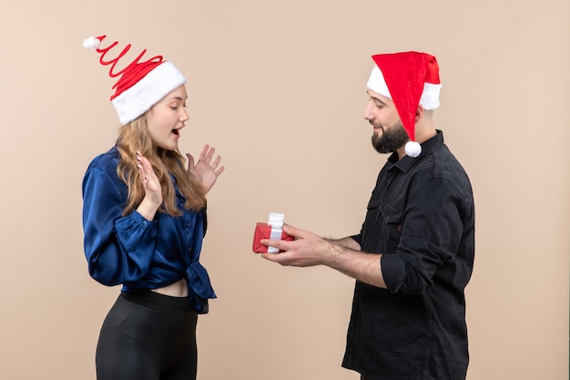 Vista frontal de la mujer joven con el hombre que se prepara para darle un regalo en la pared rosa