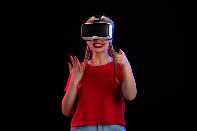 Vista frontal de la mujer joven jugando realidad virtual en la pared oscura