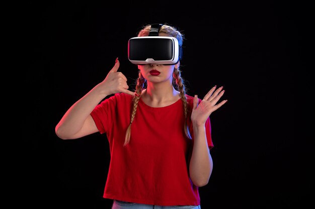 Vista frontal de la mujer joven jugando realidad virtual en la pared oscura