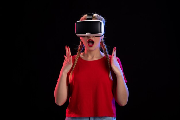 Vista frontal de la mujer joven jugando realidad virtual en la pared oscura