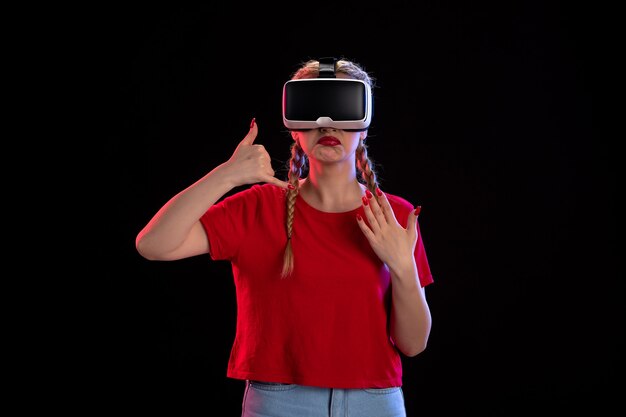 Vista frontal de la mujer joven jugando realidad virtual en la pared oscura
