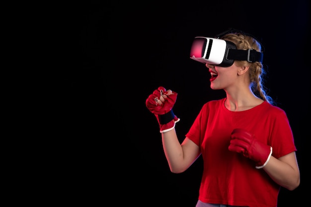 Vista frontal de la mujer joven jugando vr en guantes de mma en la pared oscura