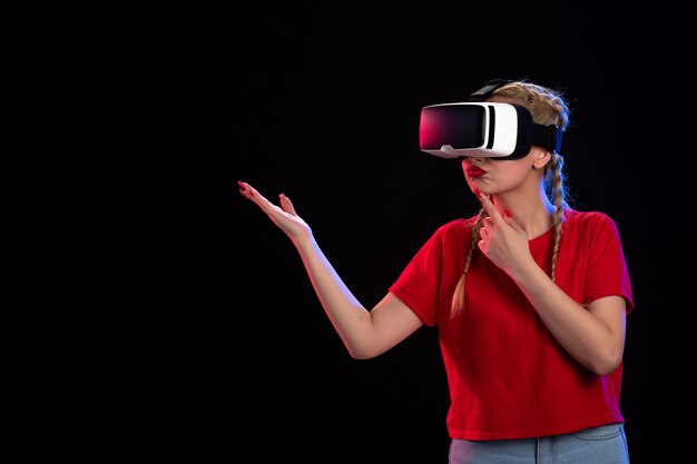 Vista frontal de la mujer joven jugando vr en la pared oscura