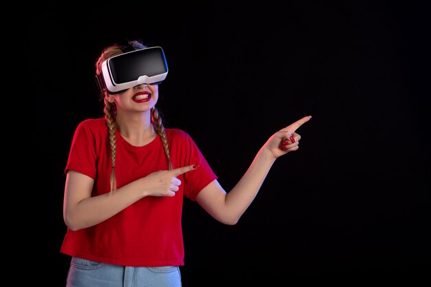 Vista frontal de la mujer joven jugando vr en la pared oscura