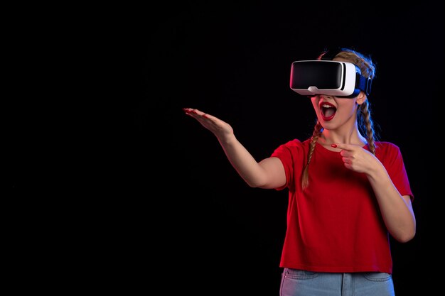 Vista frontal de la mujer joven jugando vr en la pared oscura