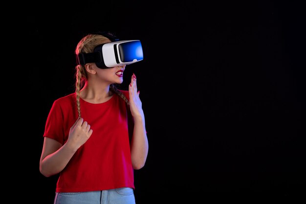 Vista frontal de la mujer joven jugando vr en la pared oscura