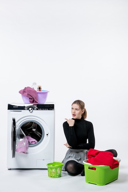 Foto gratuita vista frontal de la mujer joven con lavadora doblando ropa sucia en la pared blanca