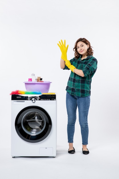 Vista frontal de la mujer joven con lavadora con guantes amarillos sobre una pared blanca