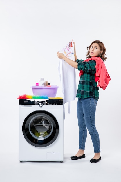 Vista frontal de la mujer joven con lavadora preparando ropa para lavar en la pared blanca