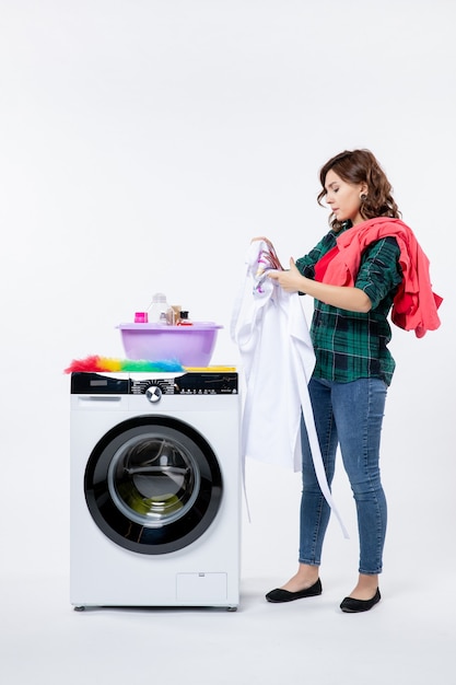 Foto gratuita vista frontal de la mujer joven con lavadora preparando ropa para lavar en la pared blanca