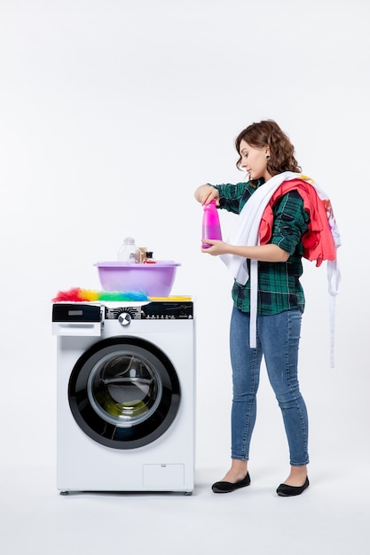 Vista frontal de la mujer joven con lavadora preparando ropa en la pared blanca