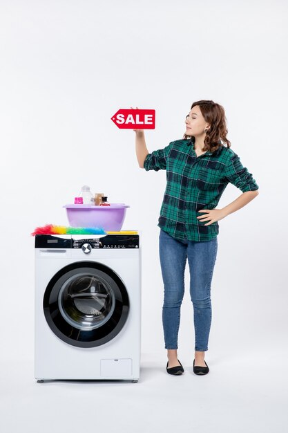 Vista frontal de la mujer joven con lavadora sosteniendo pancarta de venta en la pared blanca